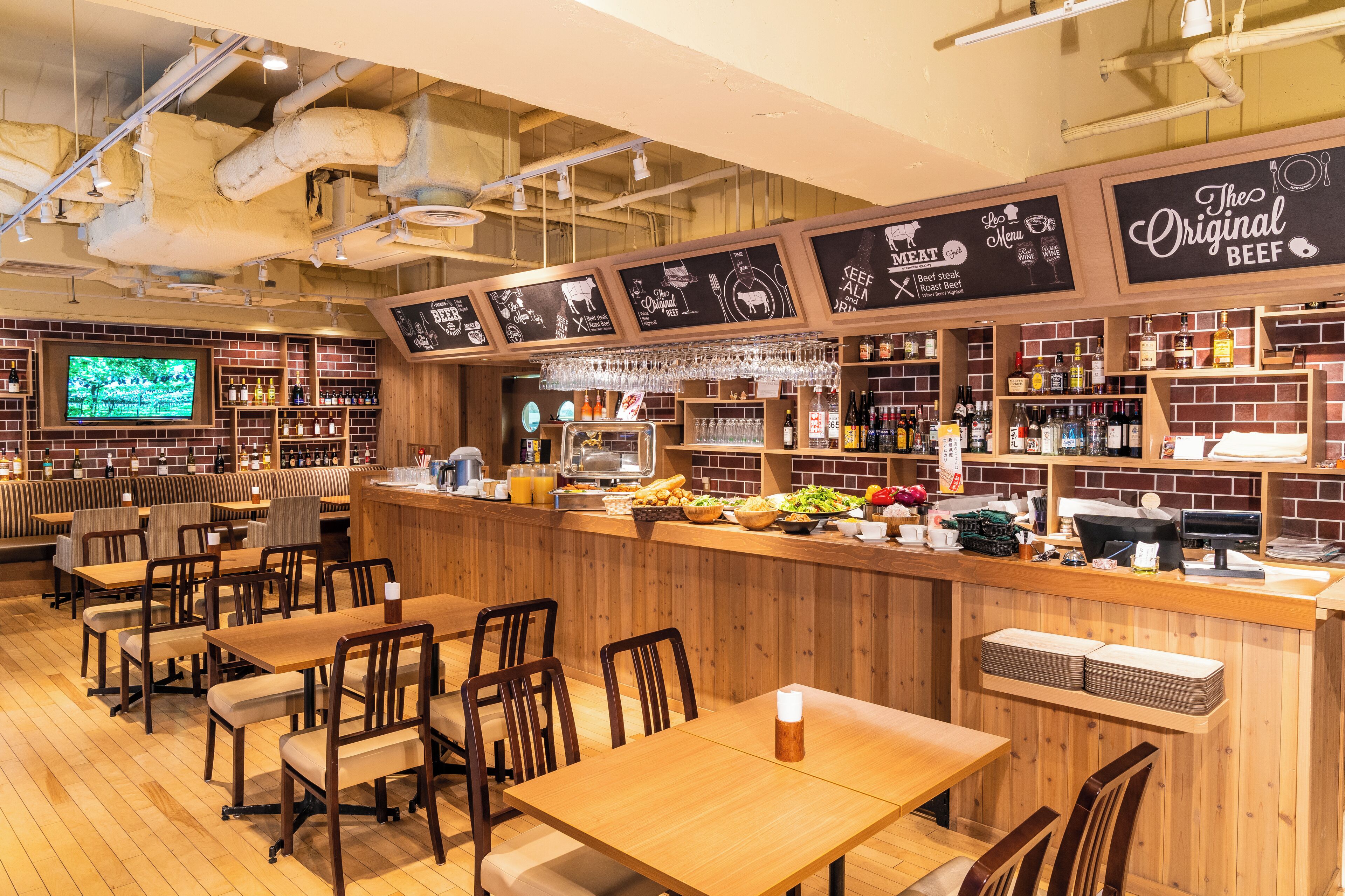 A restaurant with wooden tables and chairs, a bar area with a menu, and a television screen displaying a nature scene.