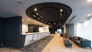 Un moderno vestíbulo de hotel con mostrador de recepción, zona de estar y un diseño de techo único.