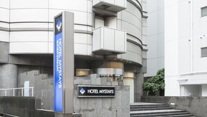 Una entrada de hotel moderna con un cartel que dice 'HOTEL MYSTAYS' y un letrero vertical azul que indica 'HOTEL MYSTAYS'.