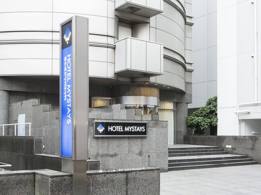 A modern hotel entrance with a sign reading "HOTEL MYSTAYS" and a blue vertical sign indicating "HOTEL MYSTAYS".
