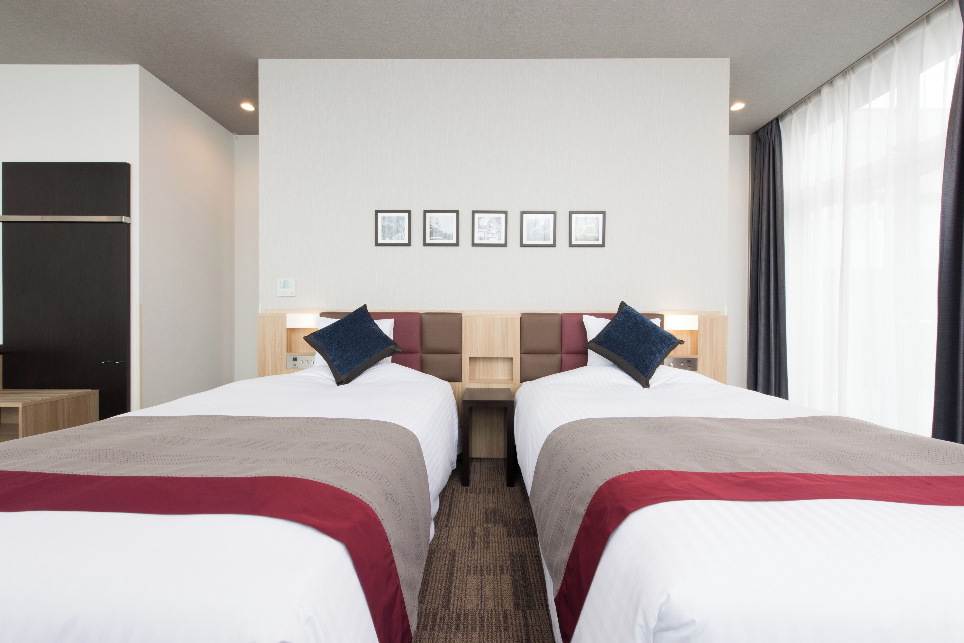 A hotel room with two beds, a wooden headboard, a small table, and a window with curtains.