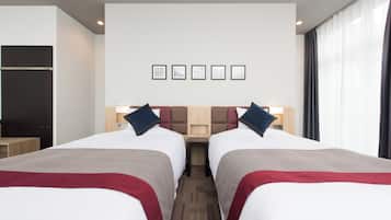 A hotel room with two beds, a wooden headboard, a small table, and a window with curtains.