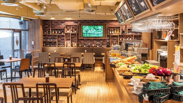 Un restaurante con mesas y sillas de madera, una zona de bar con estantes llenos de botellas y un bufé con diferentes platos.