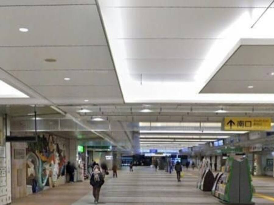 A spacious indoor corridor with overhead lighting, directional signs, and advertisements on the walls.