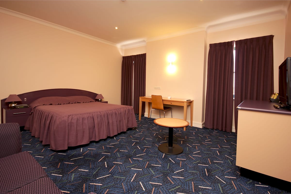 Una habitación de hotel con cama, escritorio, silla, lámpara y televisor.