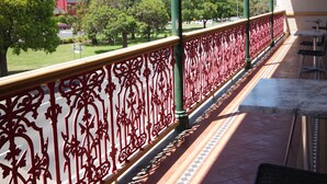 Uma varanda com grades de metal vermelhas ornamentadas, piso de azulejos e área de estar externa.
