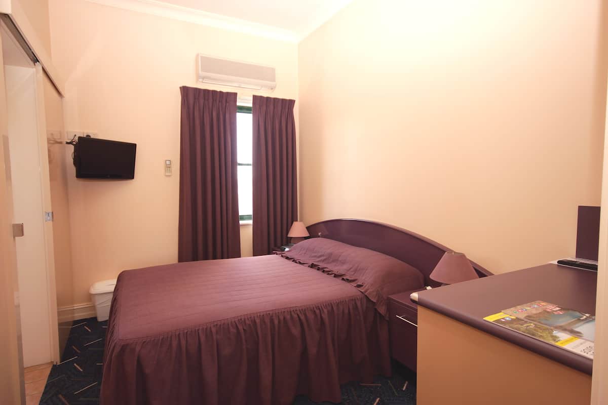 Habitación de hotel con cama, escritorio, televisión montada en la pared y ventana con cortinas.