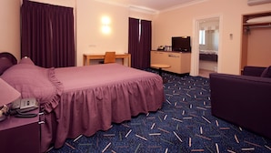Quarto de hotel com cama, escrivaninha, televisão e área de estar.