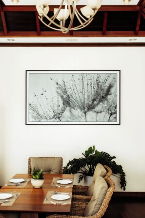 Un comedor con una mesa dispuesta para dos personas, una planta en maceta y una obra de arte abstracta enmarcada en la pared.
