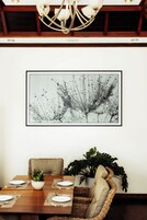 Un comedor con una mesa dispuesta para dos personas, una planta en maceta y una obra de arte abstracta enmarcada en la pared.