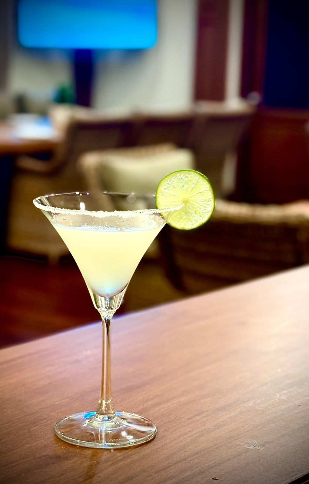 A cocktail glass with a salted rim and a lime garnish on a wooden table.