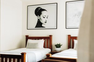 Un dormitorio con dos camas de madera, ropa de cama blanca y una planta en maceta sobre la mesita de noche.