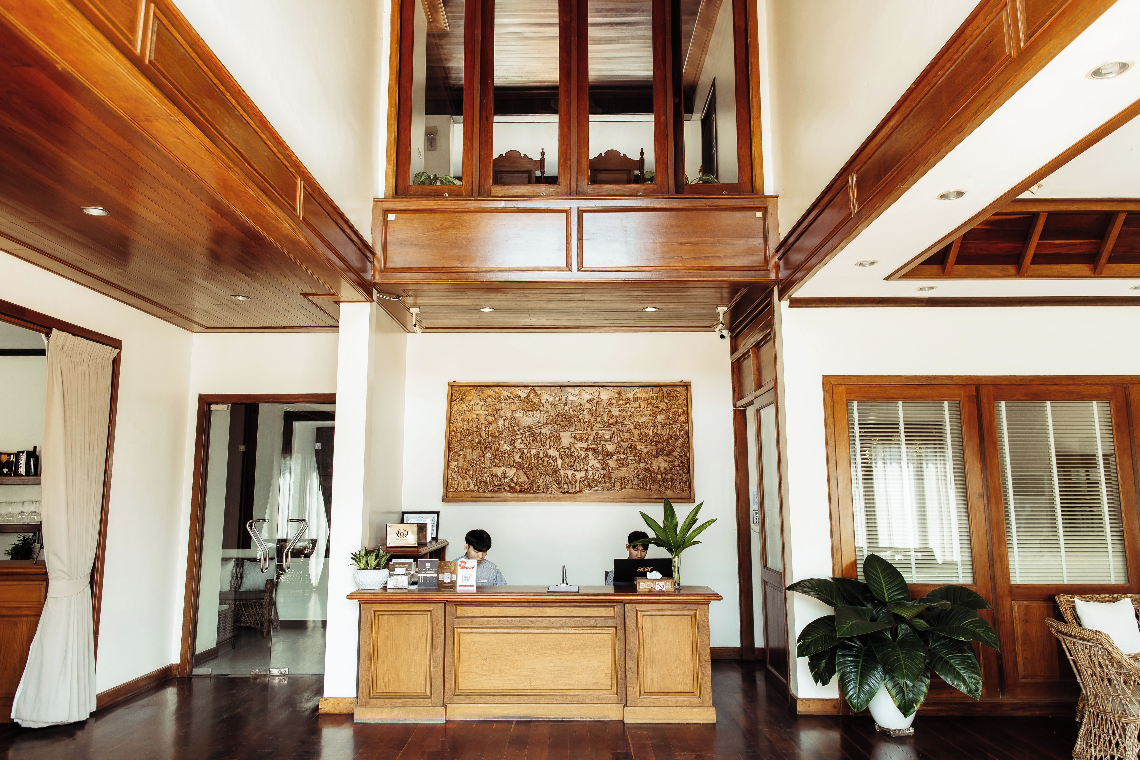A spacious lobby with a high ceiling, wooden paneling, a reception desk, and a large decorative wall piece.
