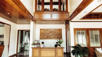 A spacious lobby with a high ceiling, wooden paneling, a reception desk, and a large decorative wall piece.