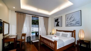 A hotel room with a wooden bed, a desk, a chair, a desk lamp, and a view of the outdoors. - Athena Hotel (Pakse)
