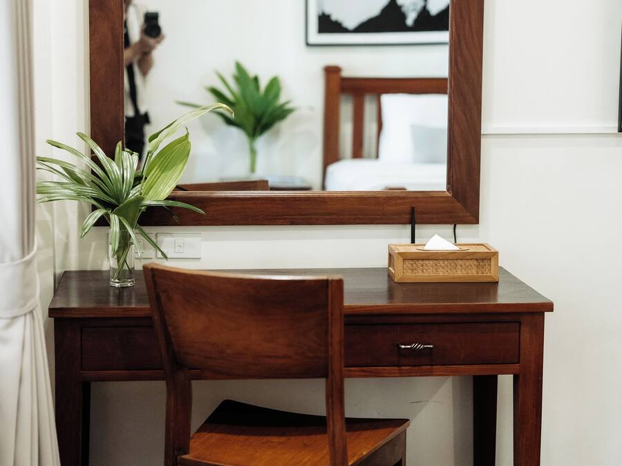 Un escritorio de madera con un espejo, una silla, un florero con hojas verdes y una cajita de madera.
