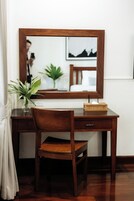 Un escritorio de madera con un espejo, una silla, un florero con hojas verdes y una cajita de madera.