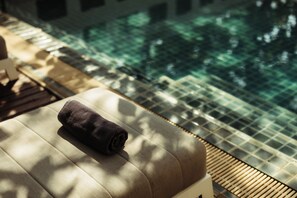 A sunlit room with a view of an indoor pool and a towel on a cushioned bench. - Athena Hotel (Pakse)