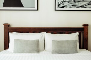 Una cama con cabecera de madera, dos almohadas y un colchón blanco.