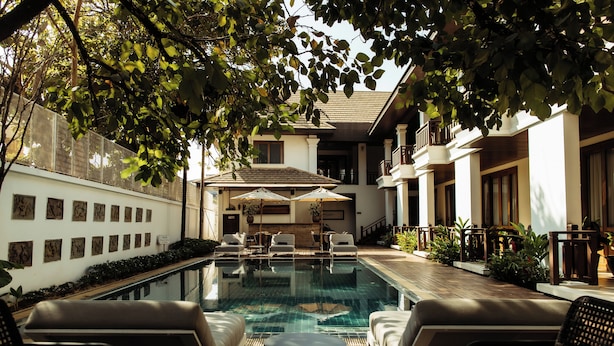 An outdoor swimming pool with lounge chairs and umbrellas, surrounded by a building with a balcony and a wall of artwork. - Athena Hotel (Pakse)