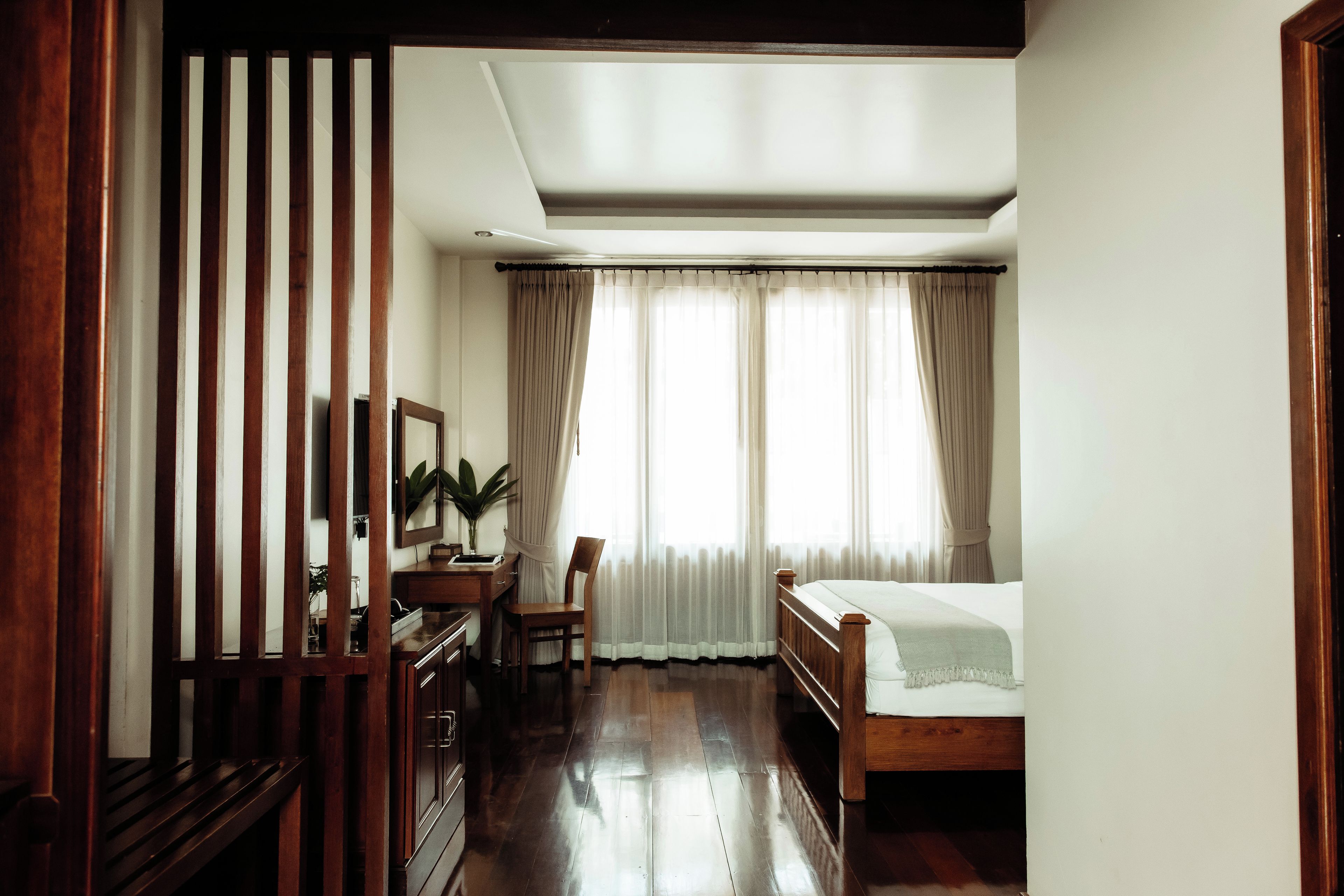 Un dormitorio con una cama de madera, un escritorio con una silla, un espejo y una planta en maceta.