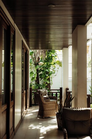 A covered porch with a wicker chair, a potted plant, and a view of a tree through a window. - Athena Hotel (Pakse)