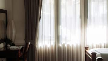A room with a wooden floor, a desk with a chair, a bed, and a window with sheer curtains.