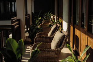 Sillas de mimbre con cojines en un porche soleado con plantas en macetas.