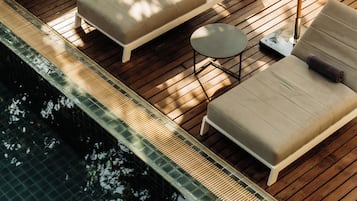 A poolside area with lounge chairs and umbrellas, a small table, and a wooden deck.