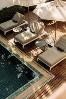 Zona junto a la piscina con sillones de descanso y sombrillas, una mesita y una terraza de madera.
