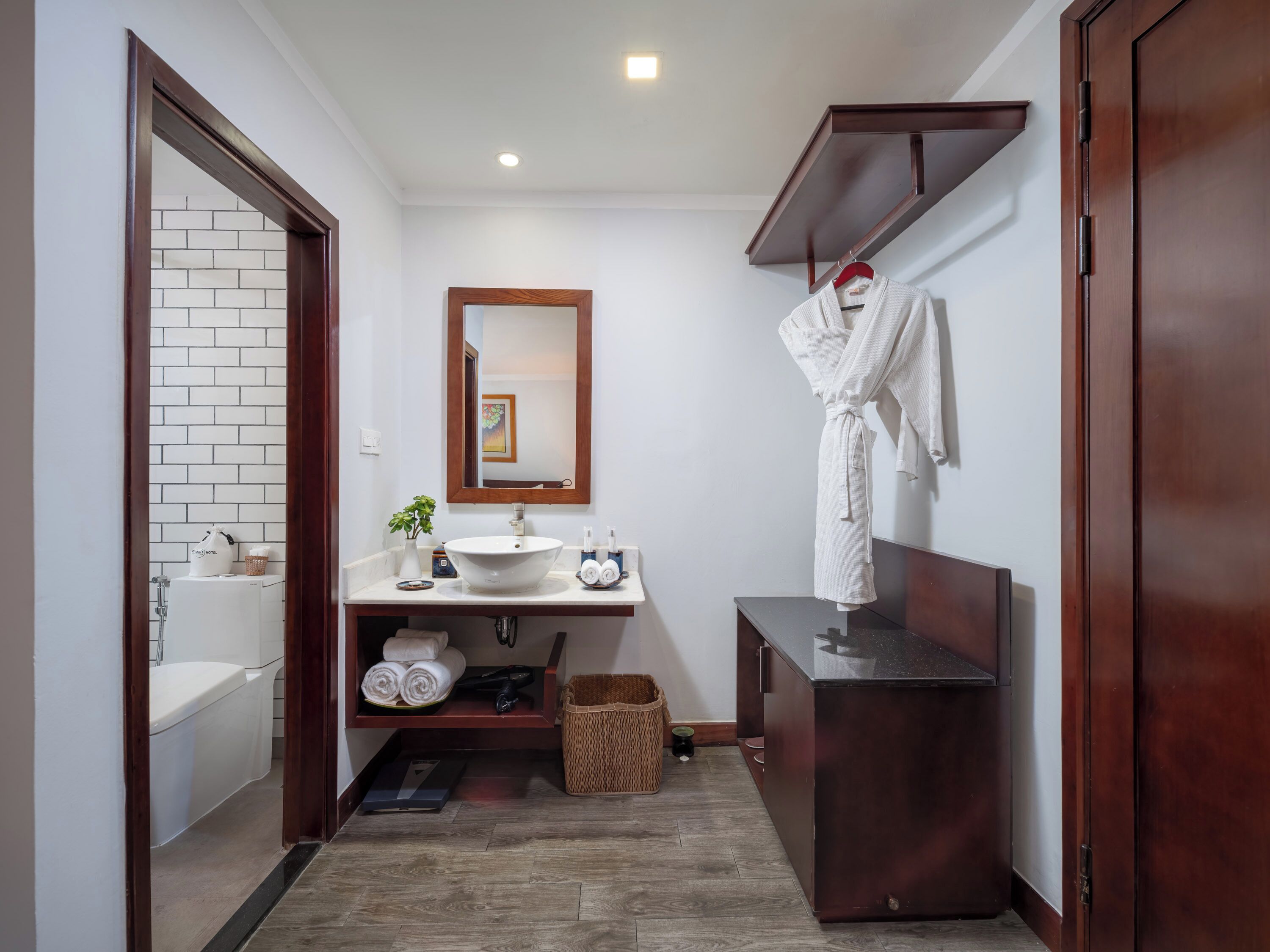 Un baño pequeño con un lavabo blanco, un espejo, un perchero para toallas y un mueble de tocador de madera.