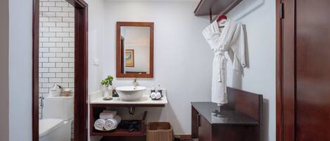 Un baño pequeño con un lavabo blanco, un espejo, un perchero para toallas y un mueble de tocador de madera.