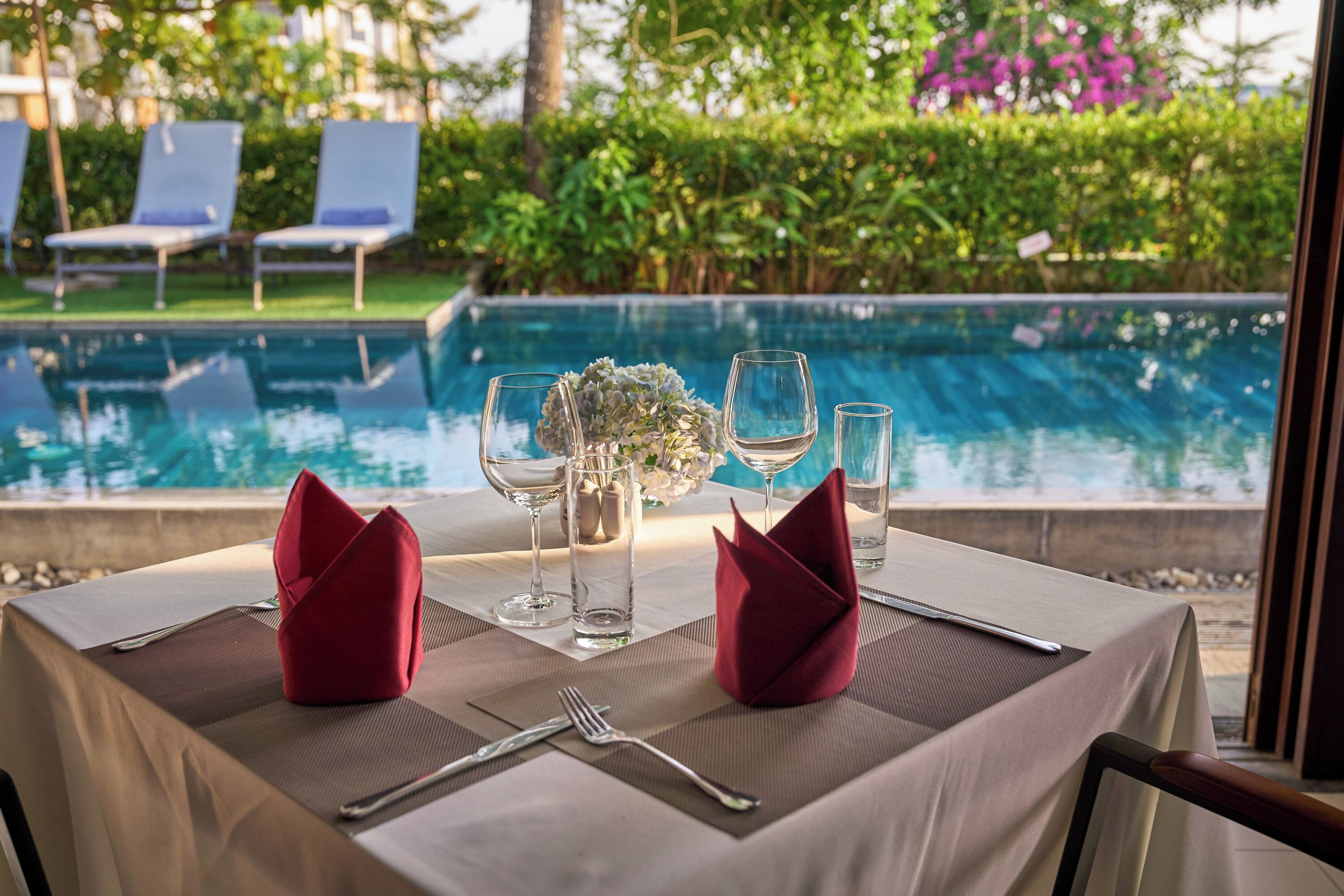 A dining table set with a white tablecloth, two red napkins, and a vase of flowers.