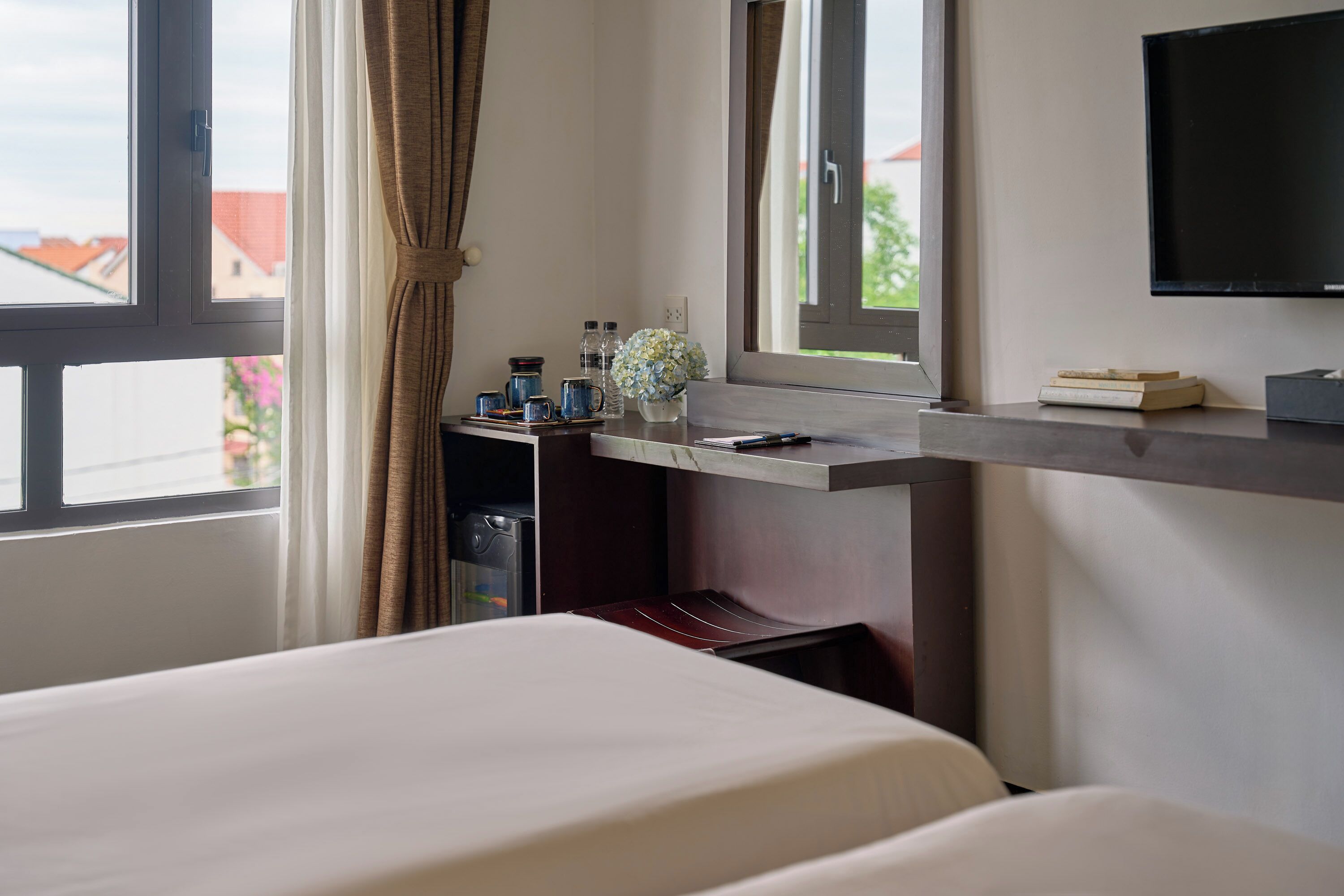 A hotel room with a bed, a desk with a computer, a TV, and a window with curtains.