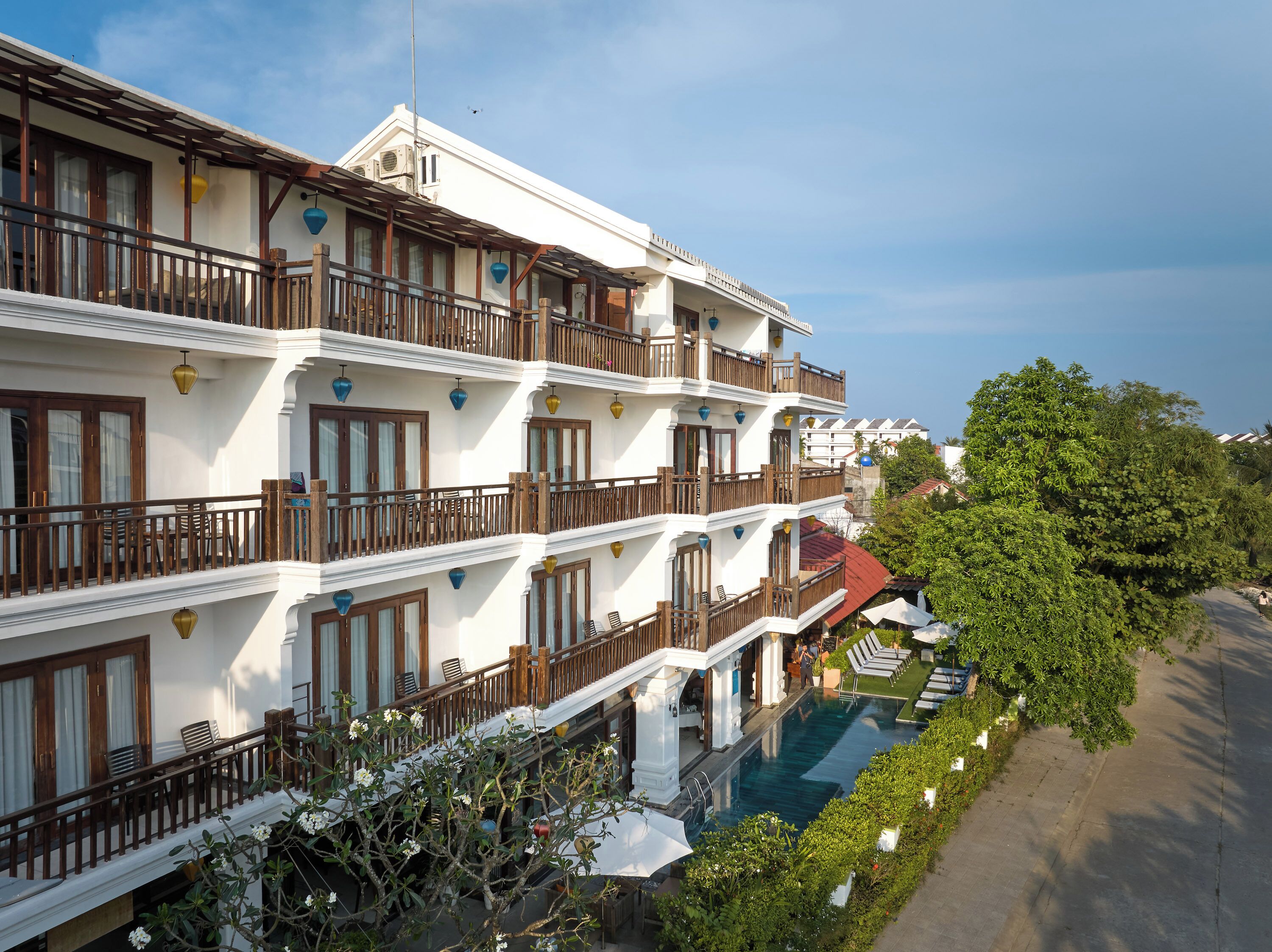 A multi-story hotel with balconies, a swimming pool, and lush greenery.