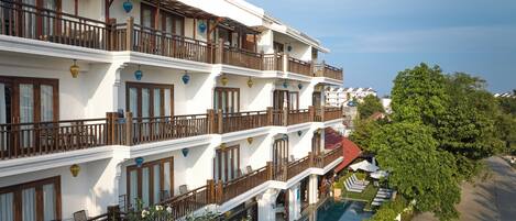 A multi-story hotel with balconies, a swimming pool, and lush greenery.