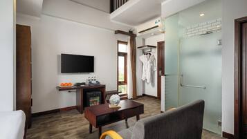 A hotel room with a wooden floor, a flat-screen TV, a small table with a vase, a sofa, and a door with a towel rack.