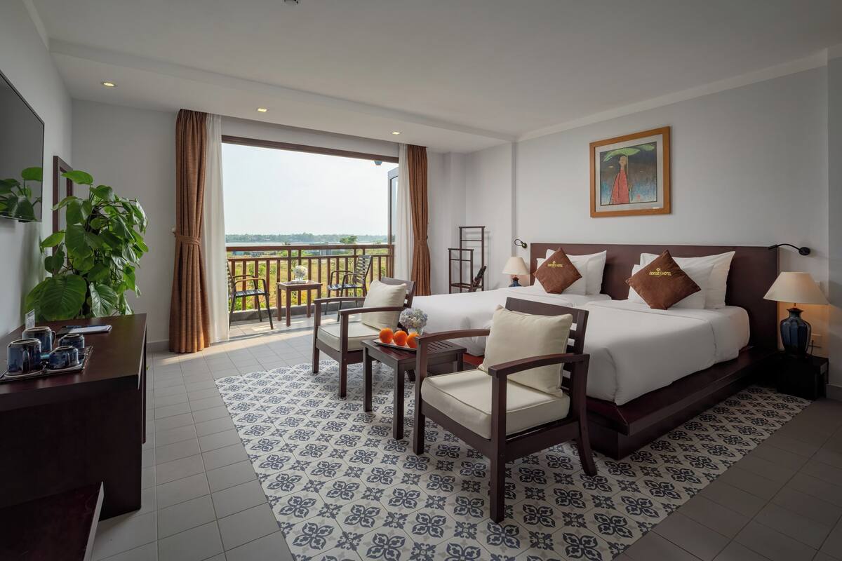 Quarto de hotel com uma cama grande, duas cadeiras, uma escrivaninha e uma varanda com vista.