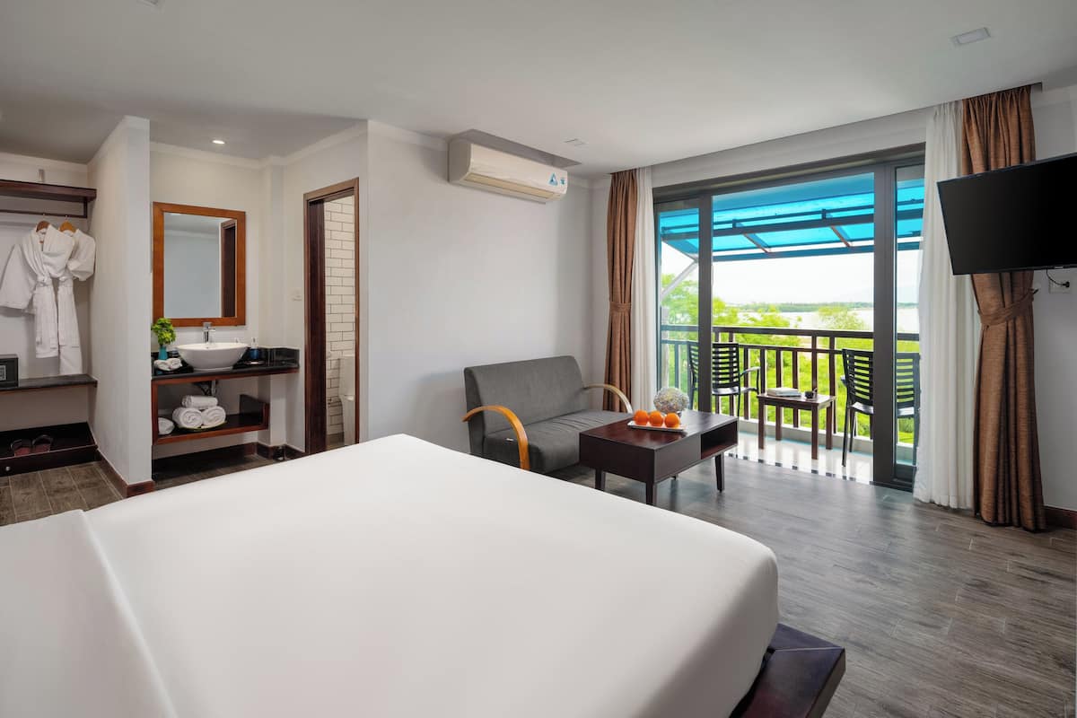 Quarto de hotel com cama, sofá, televisão, varanda com vista e banheiro com espelho e pia.