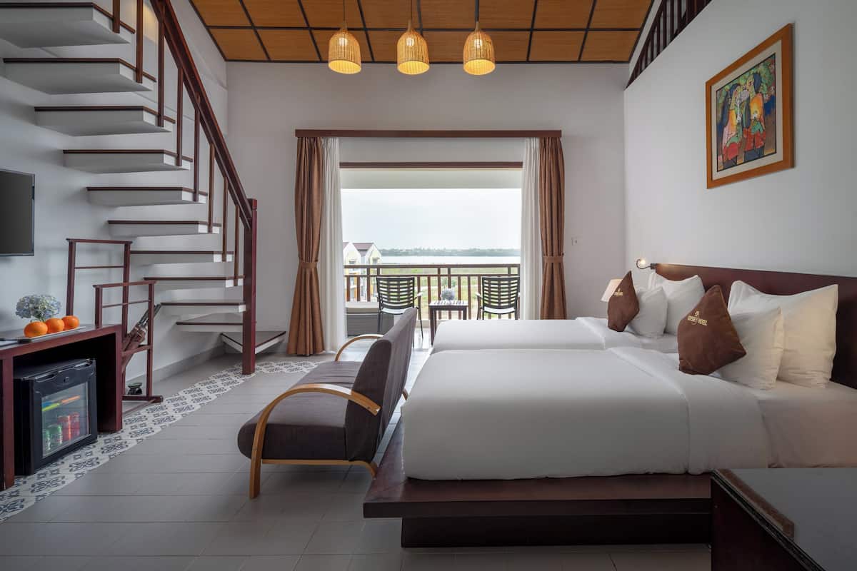 Quarto de hotel com uma cama, uma escrivaninha com computador, uma cadeira, uma televisão, uma escada e uma varanda com vista.