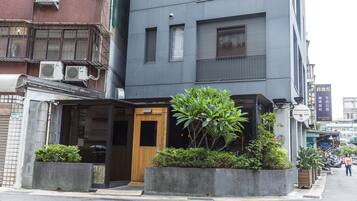 A modern building with a wooden entrance, air conditioning units, and a small garden area.