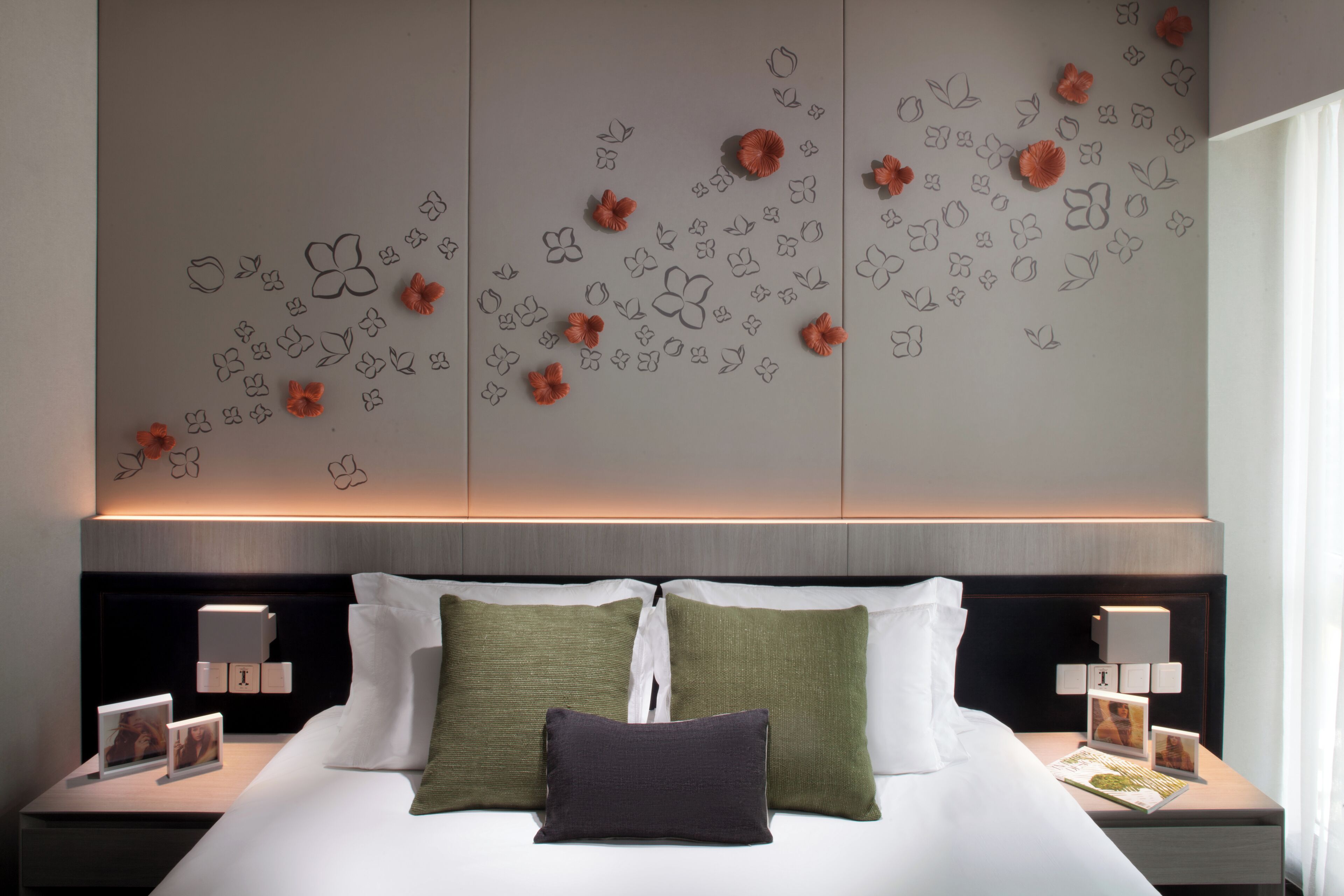 A neatly made bed with white and green pillows, a dark headboard, and a wall with decorative floral patterns.