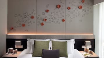 A neatly made bed with white and green pillows, a dark headboard, and a wall with decorative floral patterns.