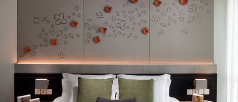 Una habitación de hotel con una cama bien hecha, dos mesitas de noche con lámparas, y una pared decorada con motivos florales y mariposas.