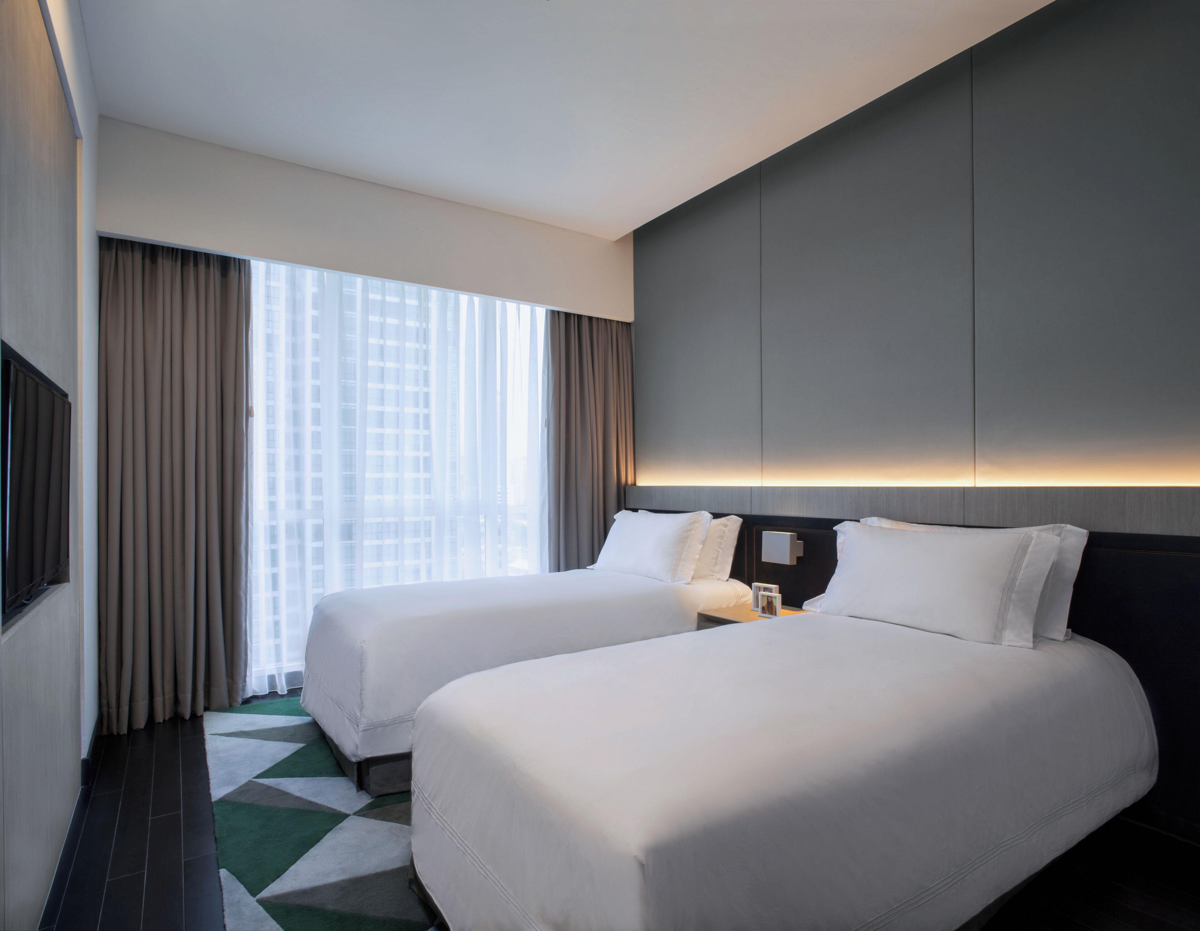 Une chambre d’hôtel avec deux lits, une grande fenêtre avec des rideaux, un téléviseur à écran plat et un design moderne.