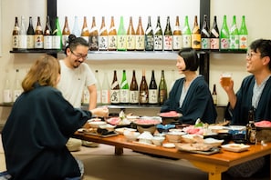 Eine Gruppe von Personen sitzt an einem Tisch mit verschiedenen Speisen und Sake-Flaschen.