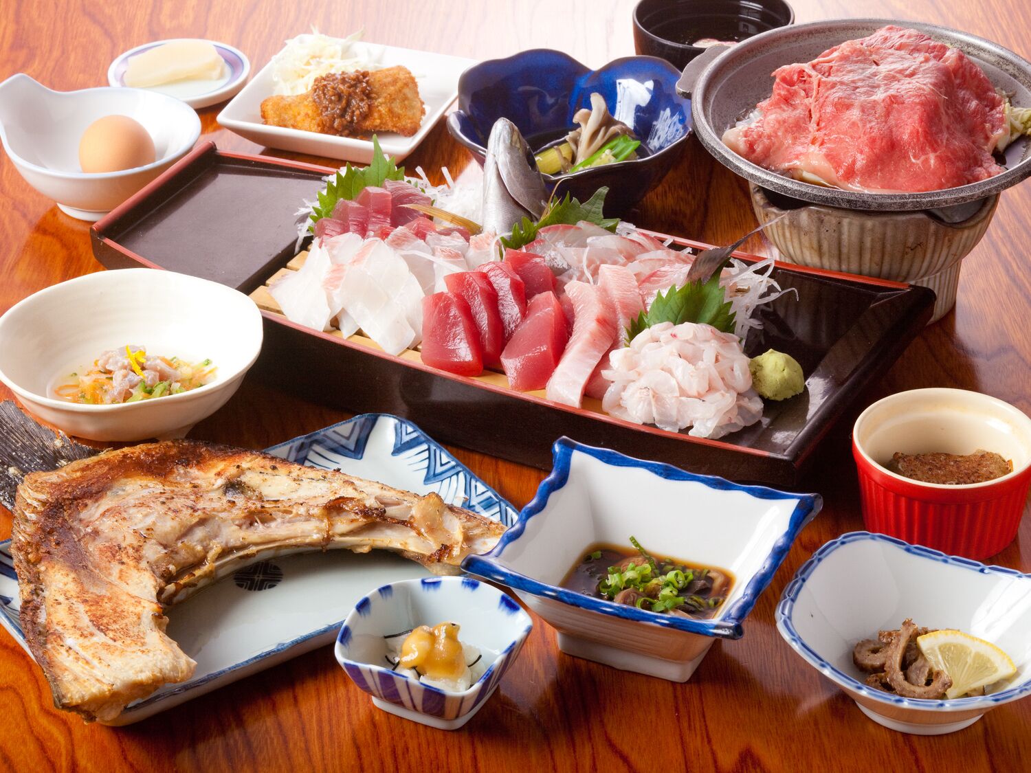 Verschiedene japanische Gerichte, darunter Sushi, Tempura und gegrillter Fisch, auf einem Holztisch serviert.