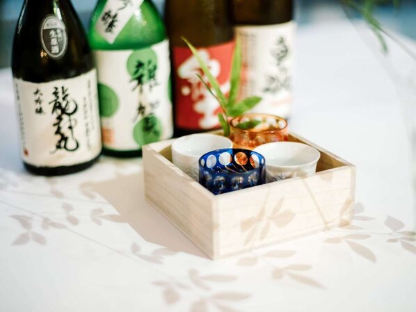 Una caja de madera con una vela azul y dos cuencos blancos, con botellas de sake al fondo.