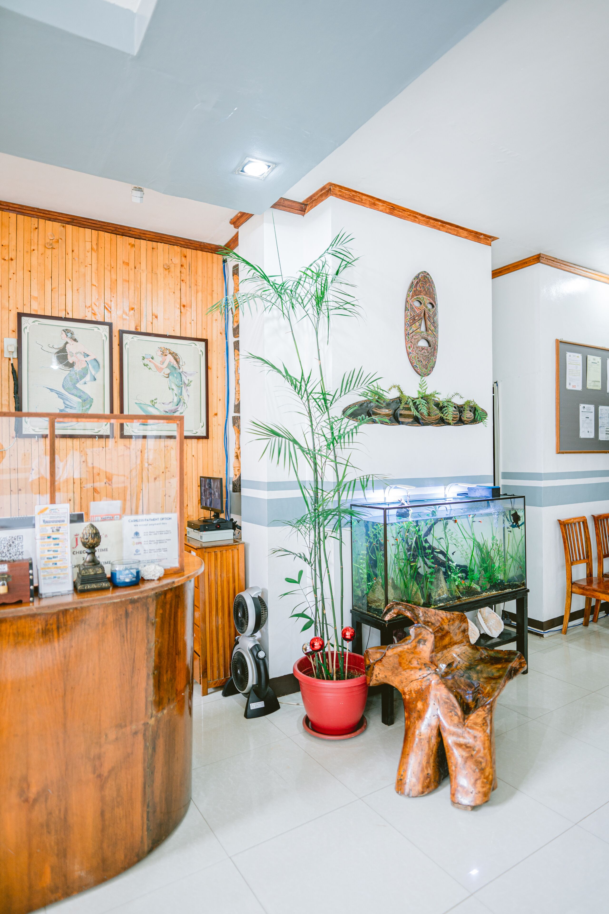 Una zona de recepción con un mostrador de madera, obras de arte enmarcadas, un acuario, plantas en macetas y una silla de madera.