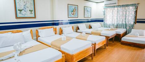 Habitación de hotel con cuatro camas individuales, cabeceras de madera, ropa de cama blanca y una pared azul a rayas.